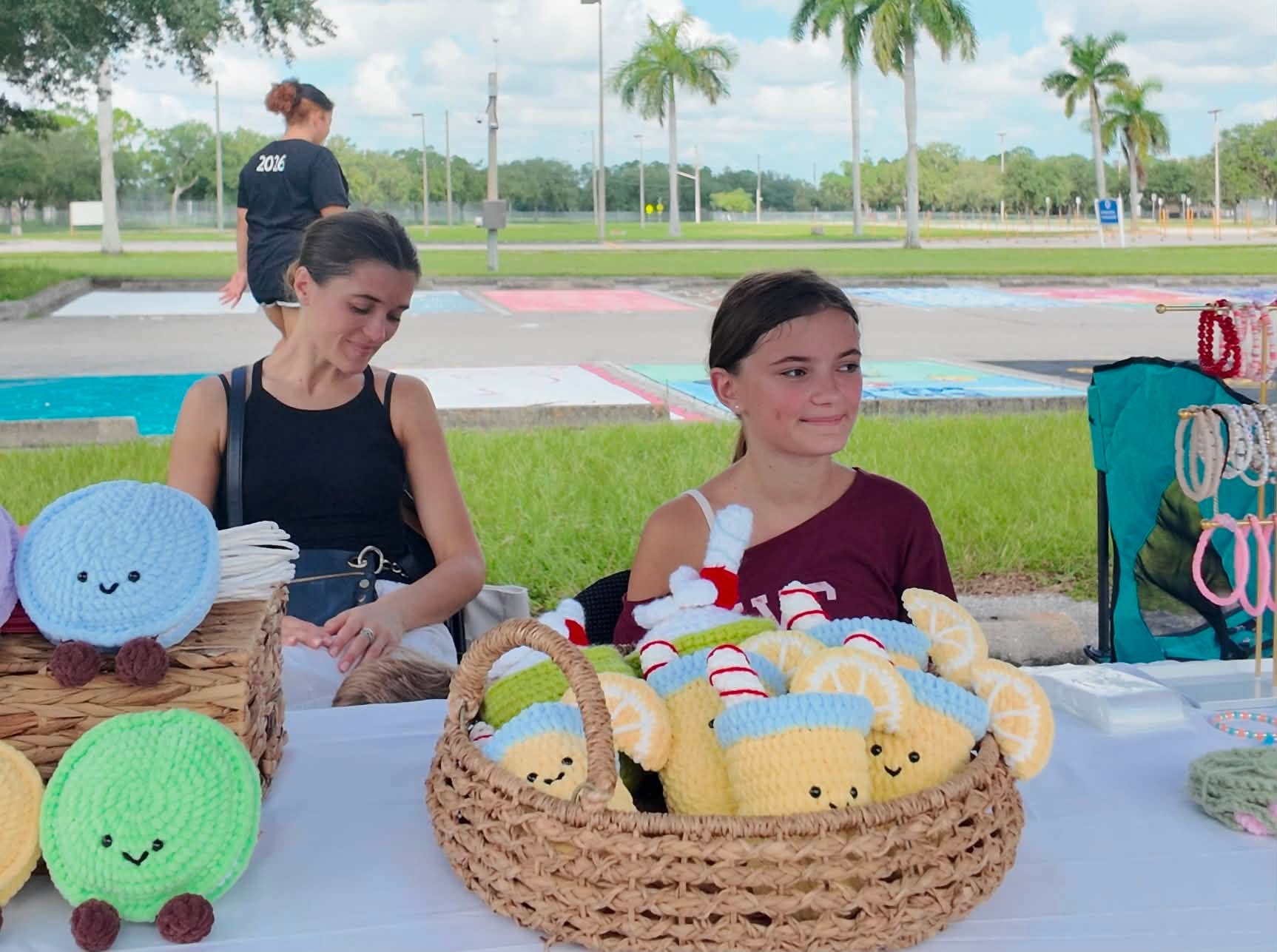 A young maker sitting with her basket of crocheted plushies at her first market stall